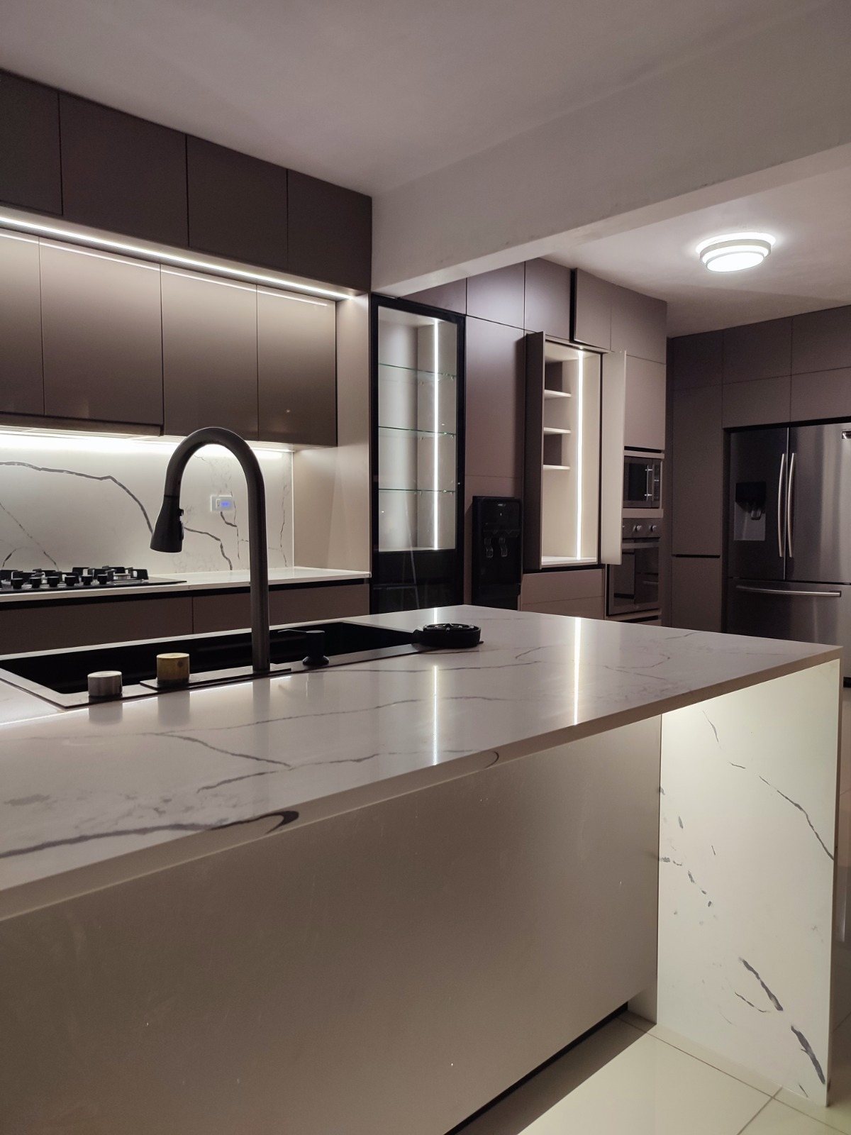 Cocina con isla de cuarzo veteado, gabinetes en gris e iluminación integrada